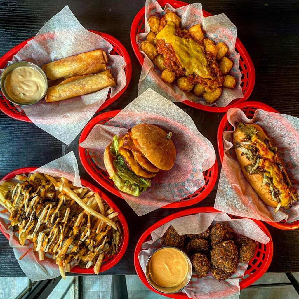 A flatlay of the plant-based restaurant in Hong Kong. There are burgers, loaded fries, cheeseburger spring rolls, chicken nuggets hot dog, and tater tots.