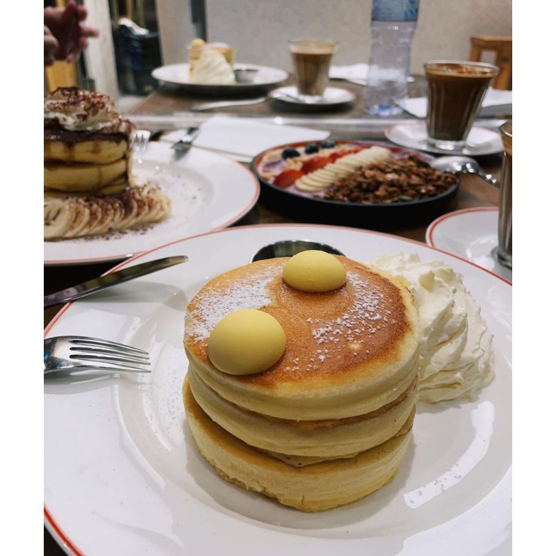 There is a stack of Elephant Grounds's OG buttermilk pancakes, with a bunch of other items from the cafe in the background.